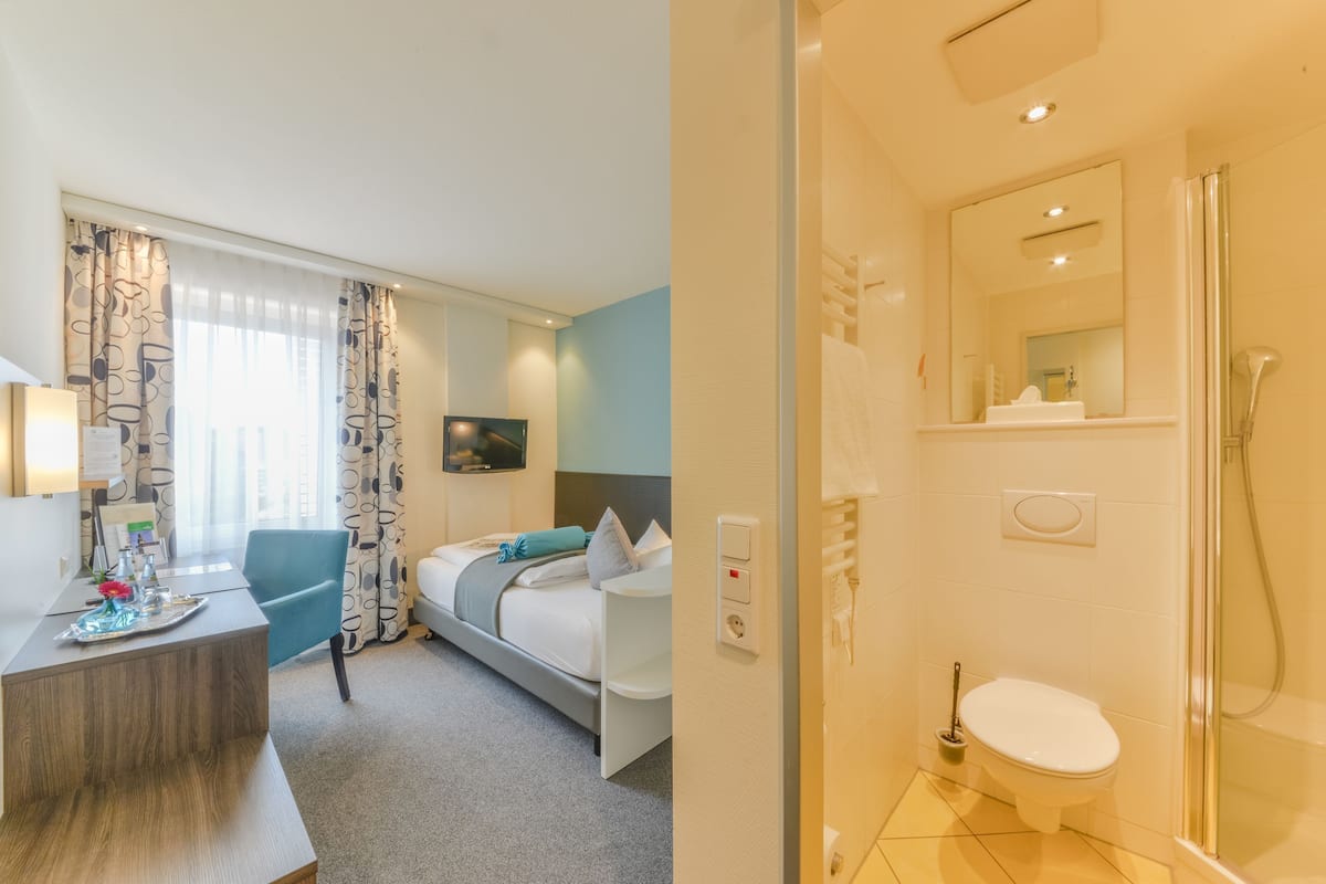 A hotel room with a desk, a bed, a shower, and a bathroom with a toilet and mirror.