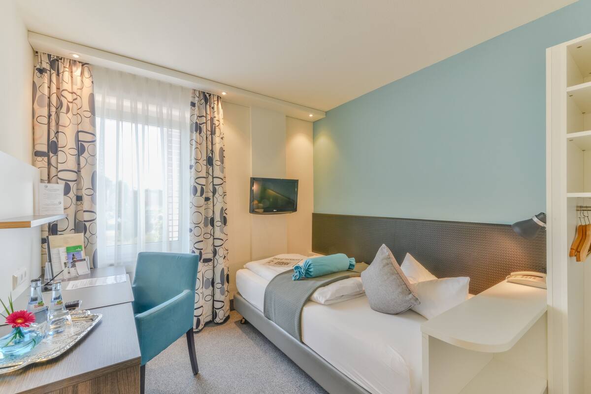 A hotel room with a bed, a desk, a chair, and a TV.