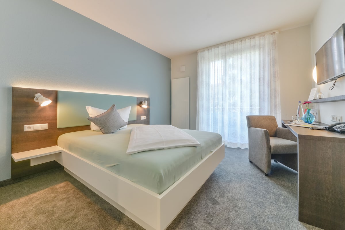 A modern hotel room with a large bed, bedside tables, a desk, and a chair.