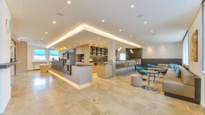 A modern hotel lobby with a central reception desk, seating area, and a bar.