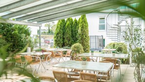 An outdoor patio area with tables and chairs, surrounded by greenery and a building with a spiral staircase.