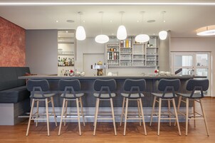 Un espace bar moderne doté d’un comptoir, de plusieurs tabourets et d’un éclairage suspendu.