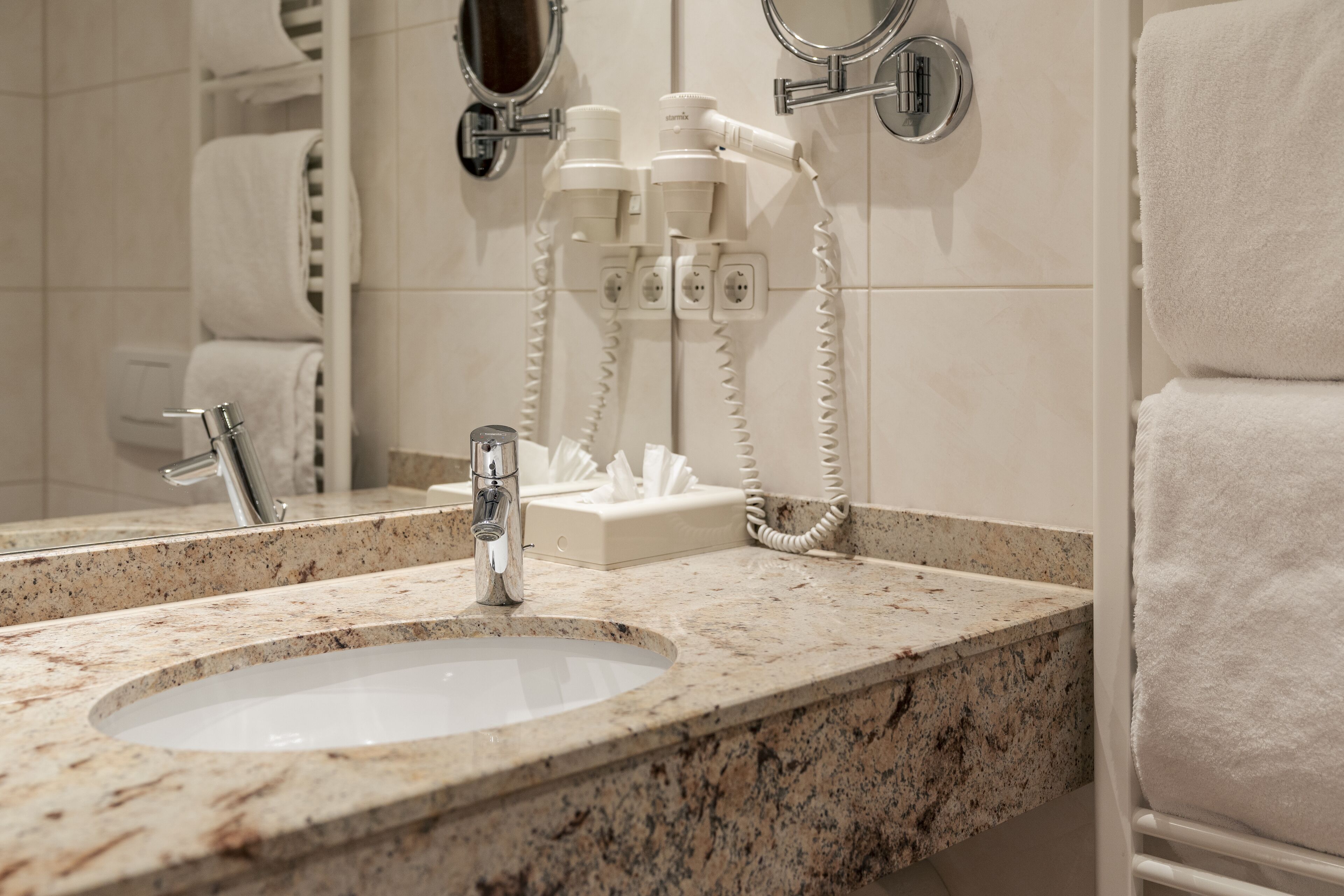 A bathroom with a granite countertop sink, a mirror, a towel rack, and a hairdryer.