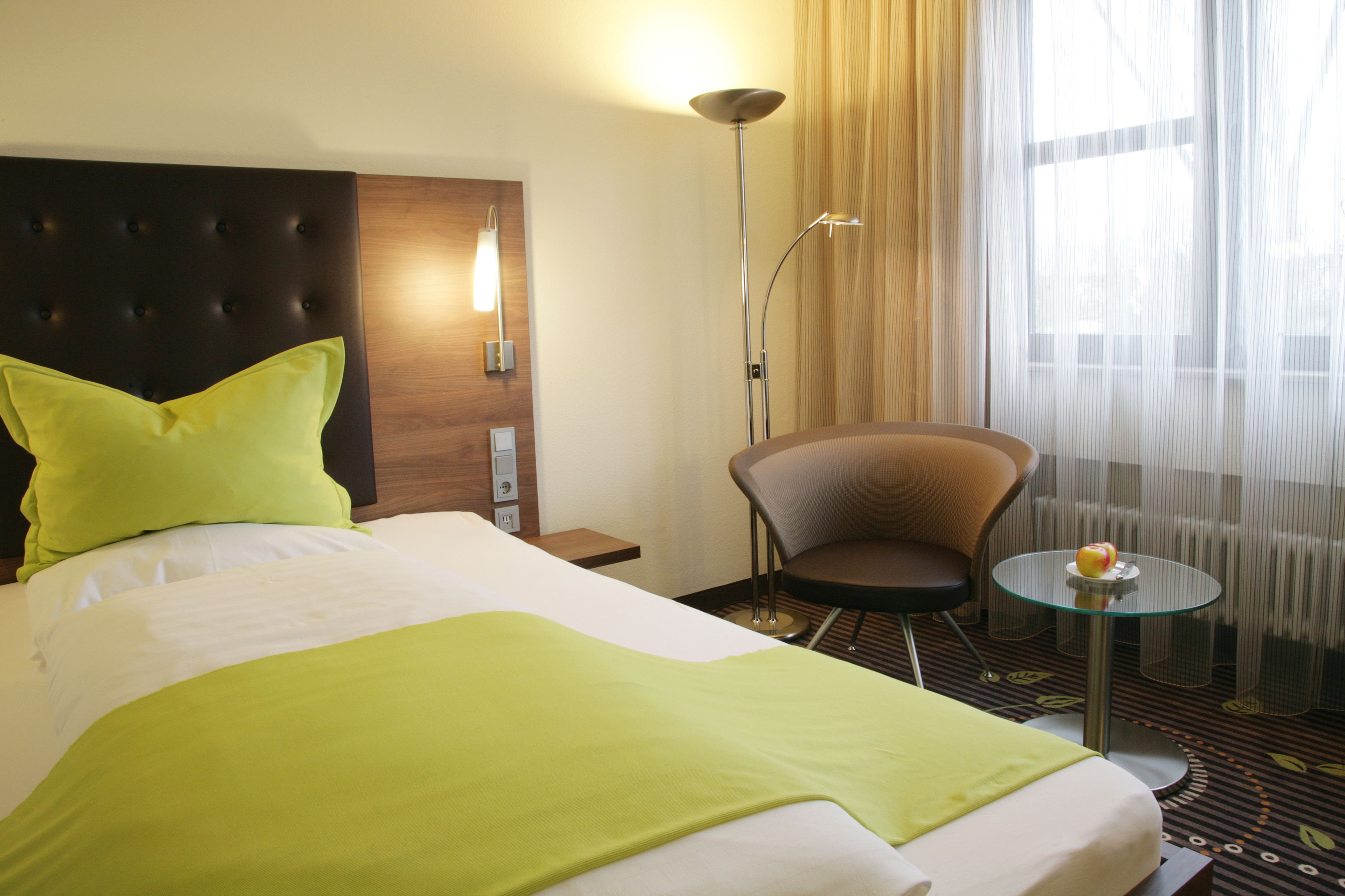 Ein Hotelzimmer mit Bett, einem Sessel, einem kleinen Tisch und einer Lampe.