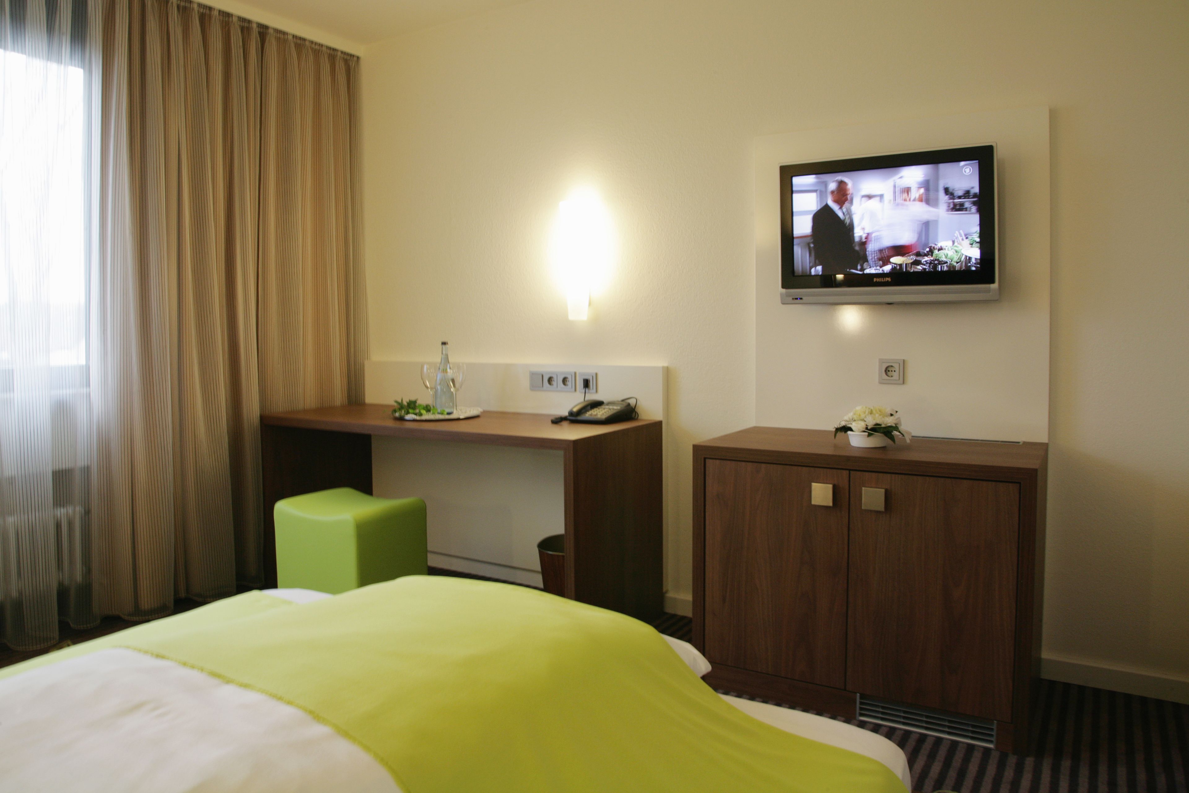 Una habitación de hotel con cama, escritorio, televisor y armario.