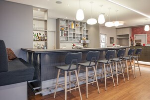 Uma área de bar moderna com balcão, banquetas e prateleiras repletas de garrafas e copos.