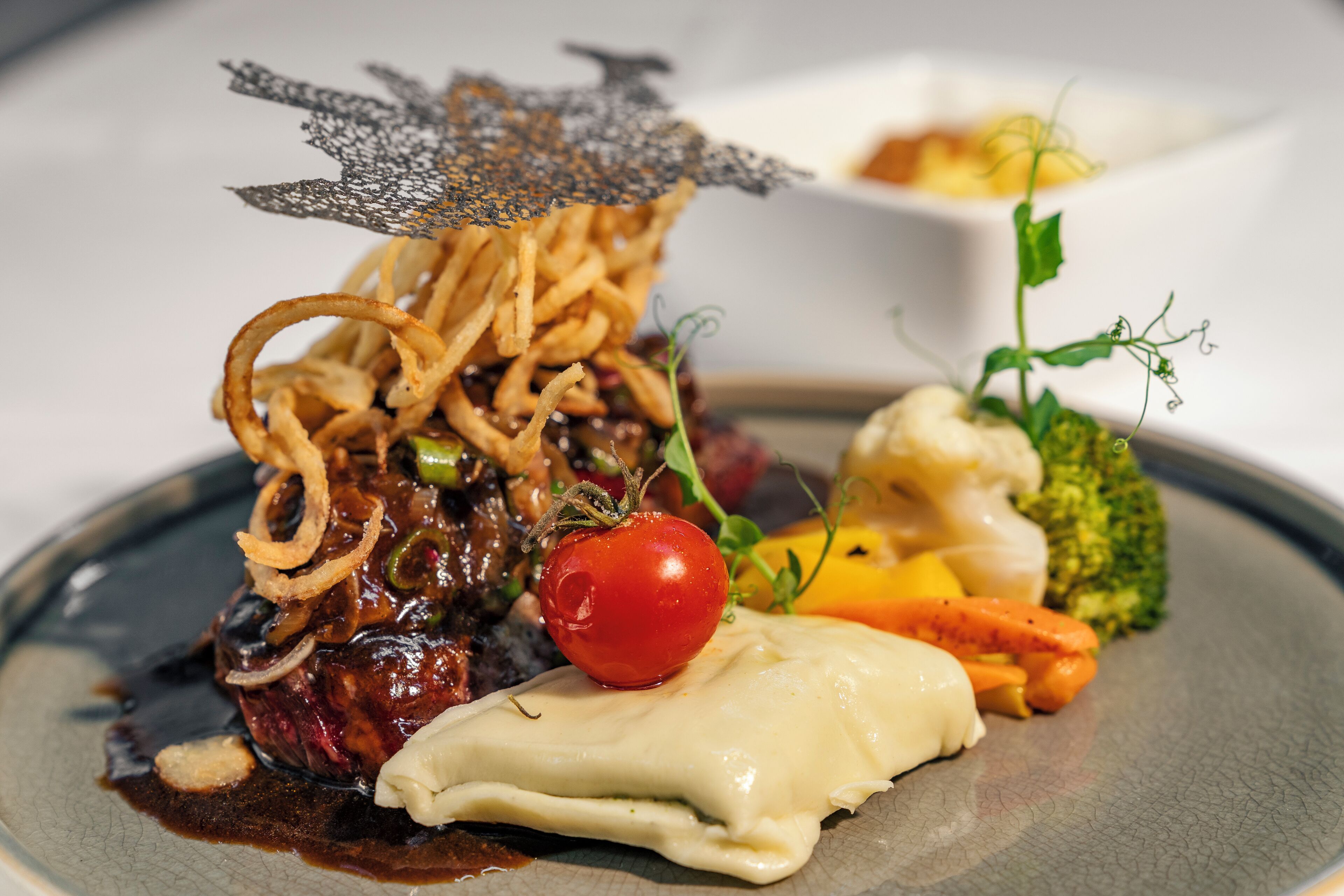 A plated dish with steak, vegetables, and a decorative element.