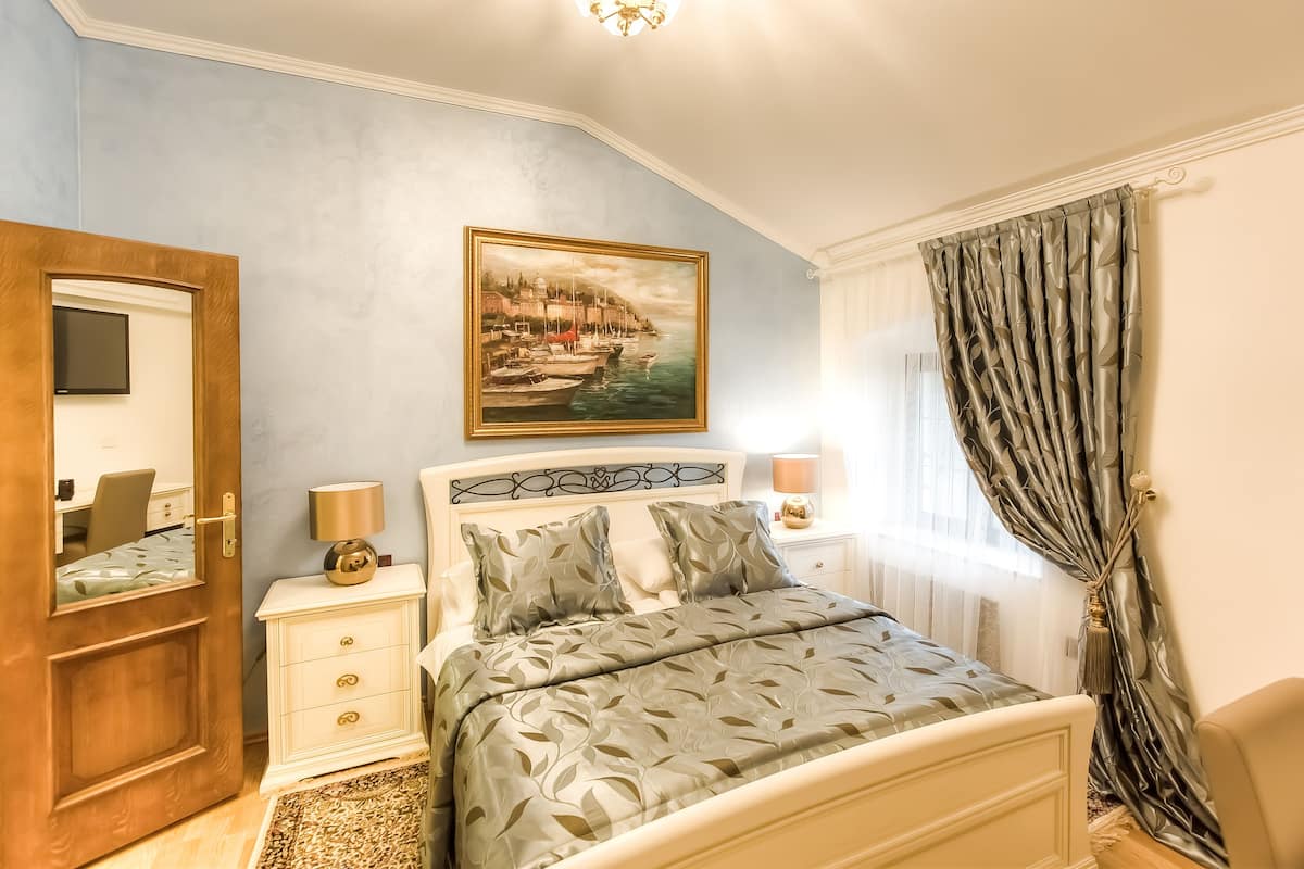 A bedroom with a bed, bedside tables, a painting, and a window with curtains.