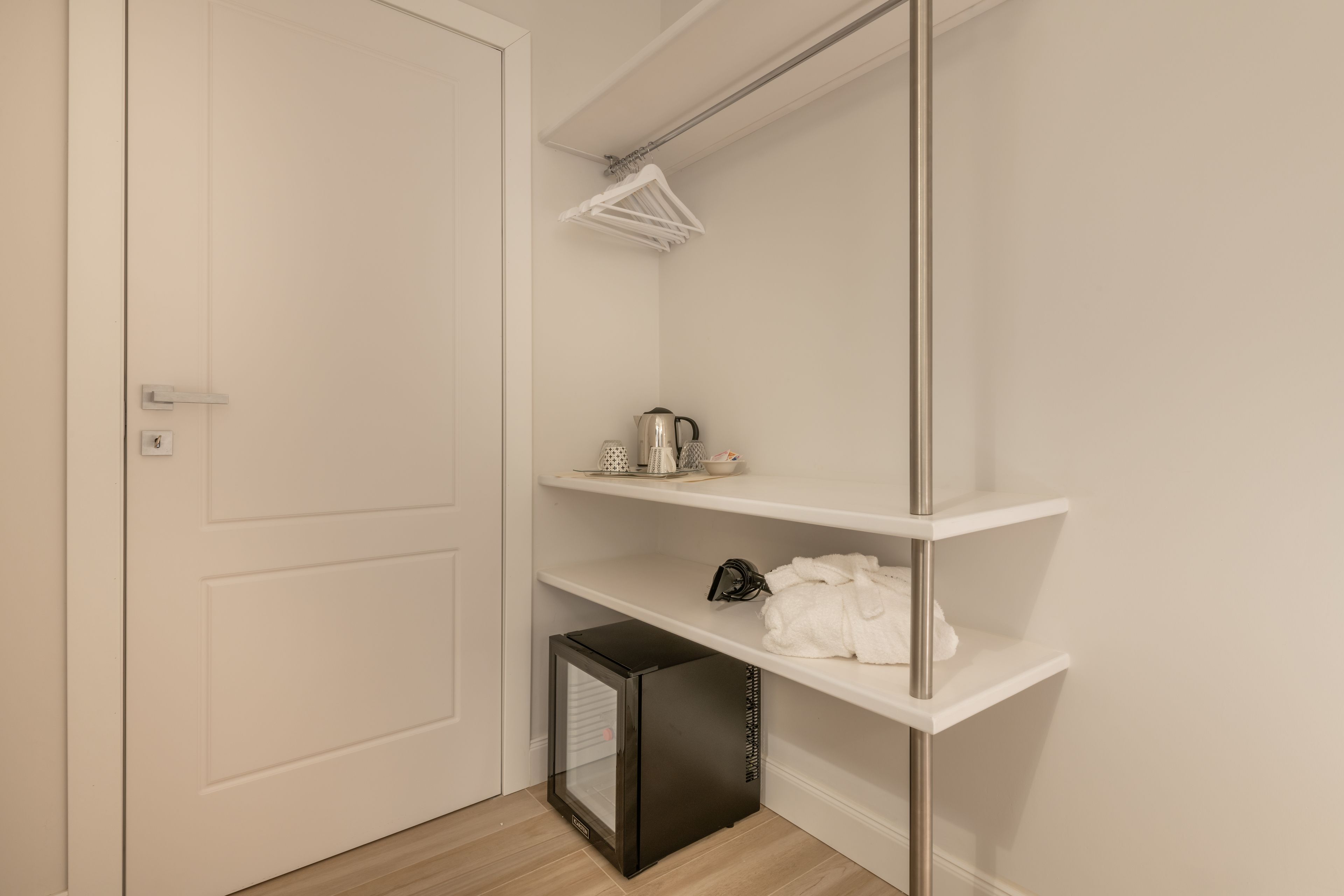 A small, neatly organized closet with white shelves, a hanging rack, and a compact heater.