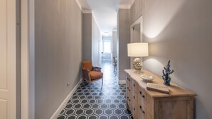 Un pasillo con piso de diseño geométrico, un aparador de madera con una lámpara y una silla.
