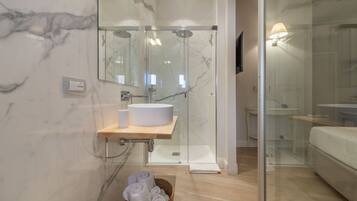A modern bathroom with a glass shower enclosure, a marble-tiled wall, a wooden vanity with a sink, and a wicker basket with towels.