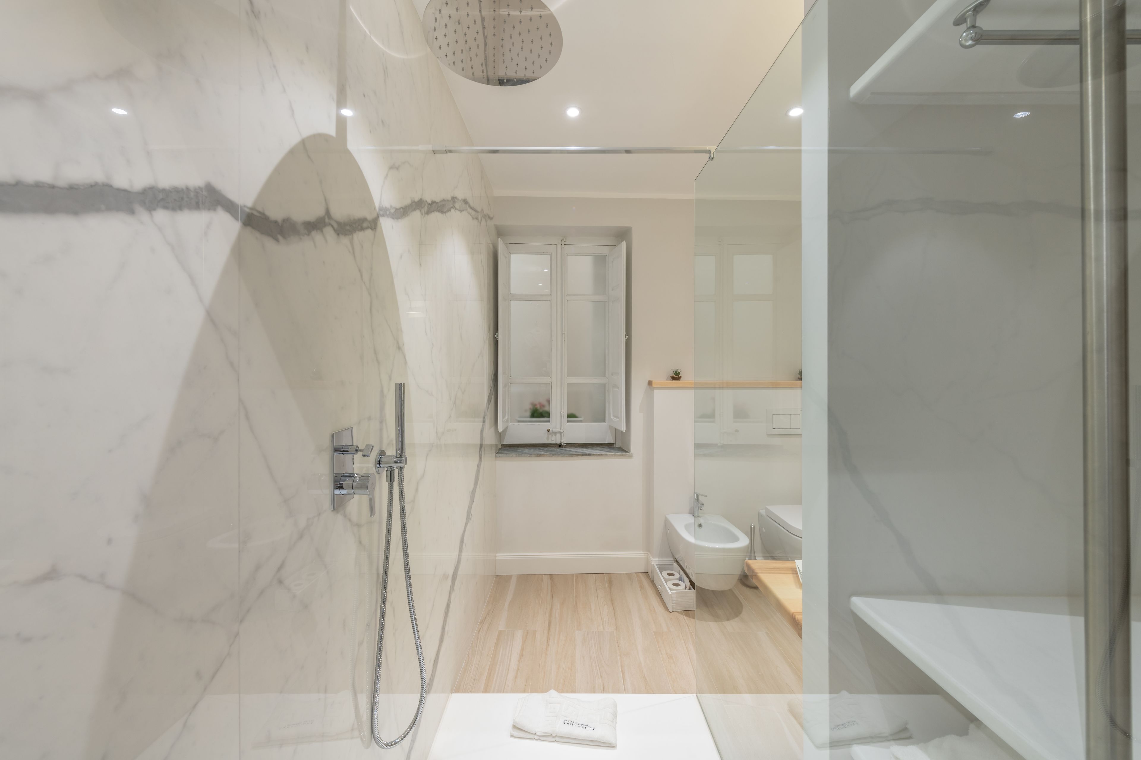 A modern bathroom with a glass shower enclosure, a marble wall, a toilet, and a sink.