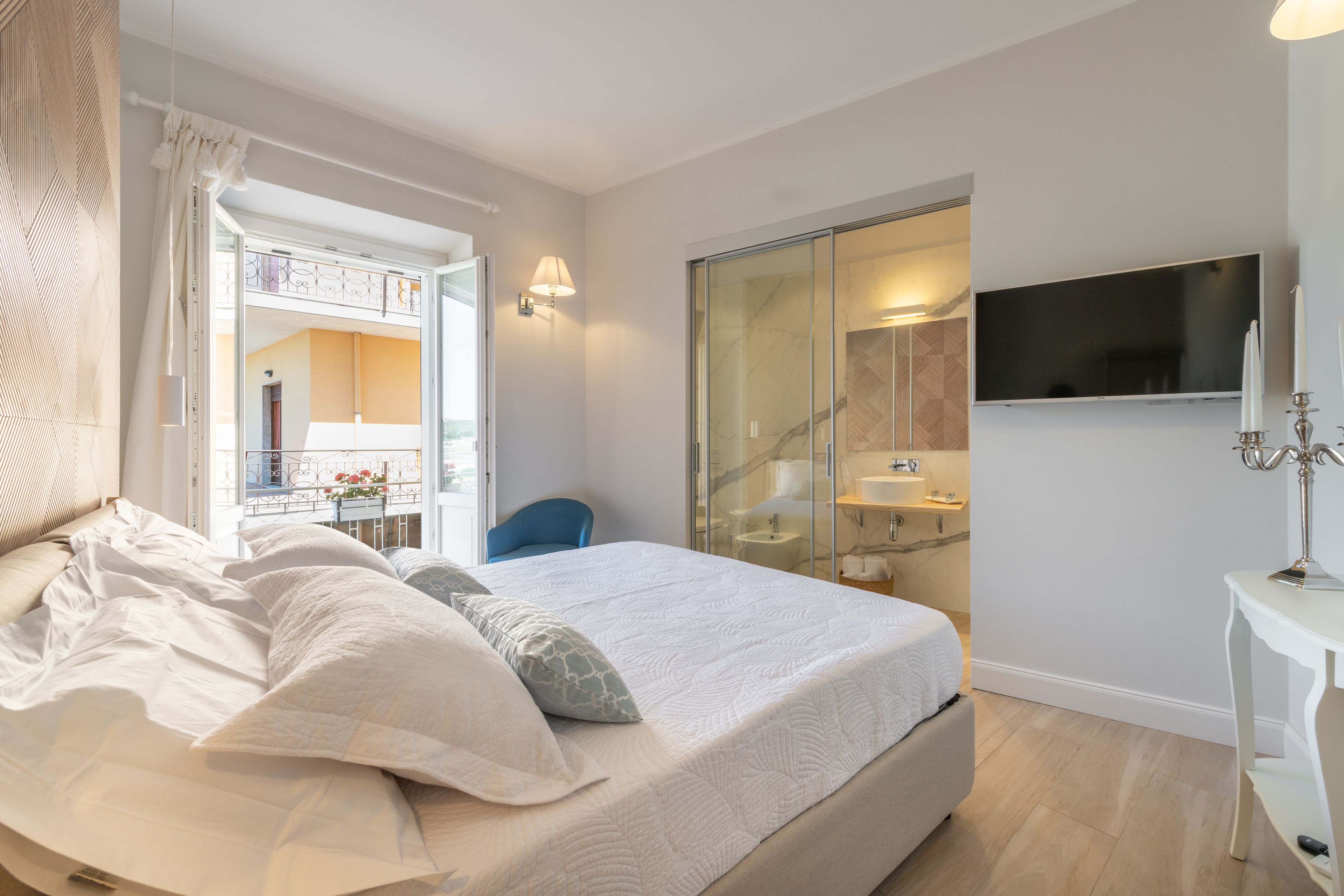 Une chambre dotée d’un grand lit, d’un téléviseur fixé au mur, d’une salle de bain avec une porte en verre et d’un balcon offrant une vue dégagée.