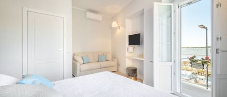 A bedroom with a large bed, a sofa, a TV, and a window with a view of the sea.