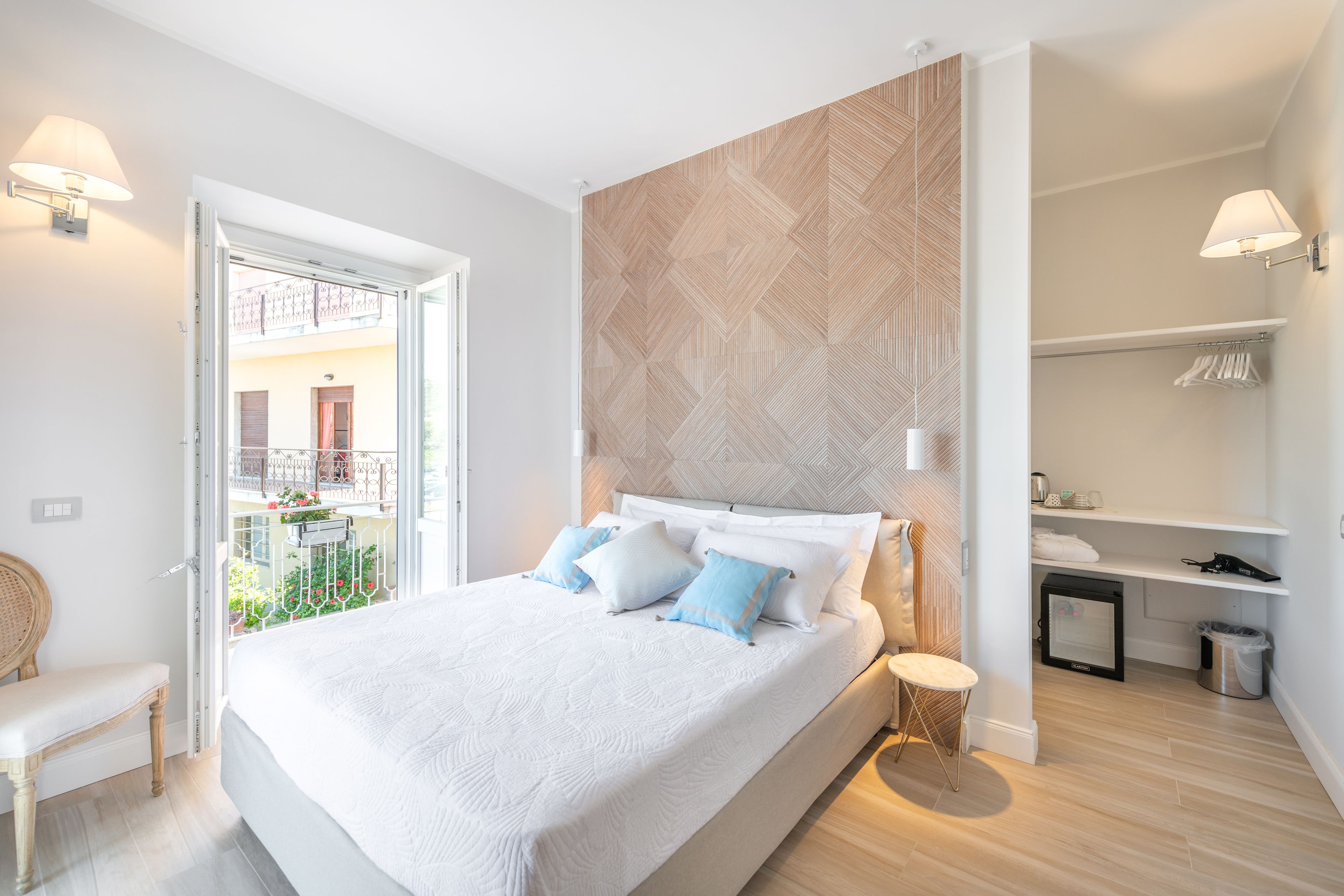 A modern bedroom with a large bed, bedside tables, a built-in wardrobe, and a view of the outside balcony.