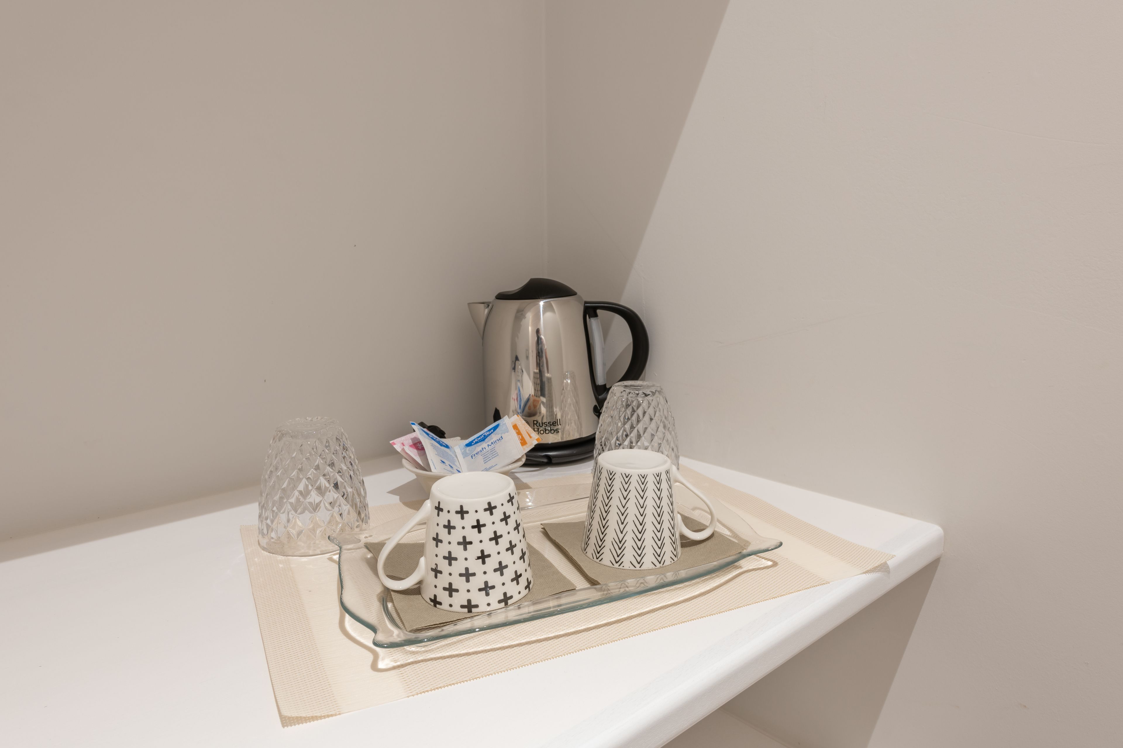 Una estantería con una tetera, dos tazas decoradas y dos vasos de vidrio sobre una bandeja.