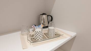 Una estantería con una tetera, dos tazas decoradas y dos vasos de vidrio sobre una bandeja.