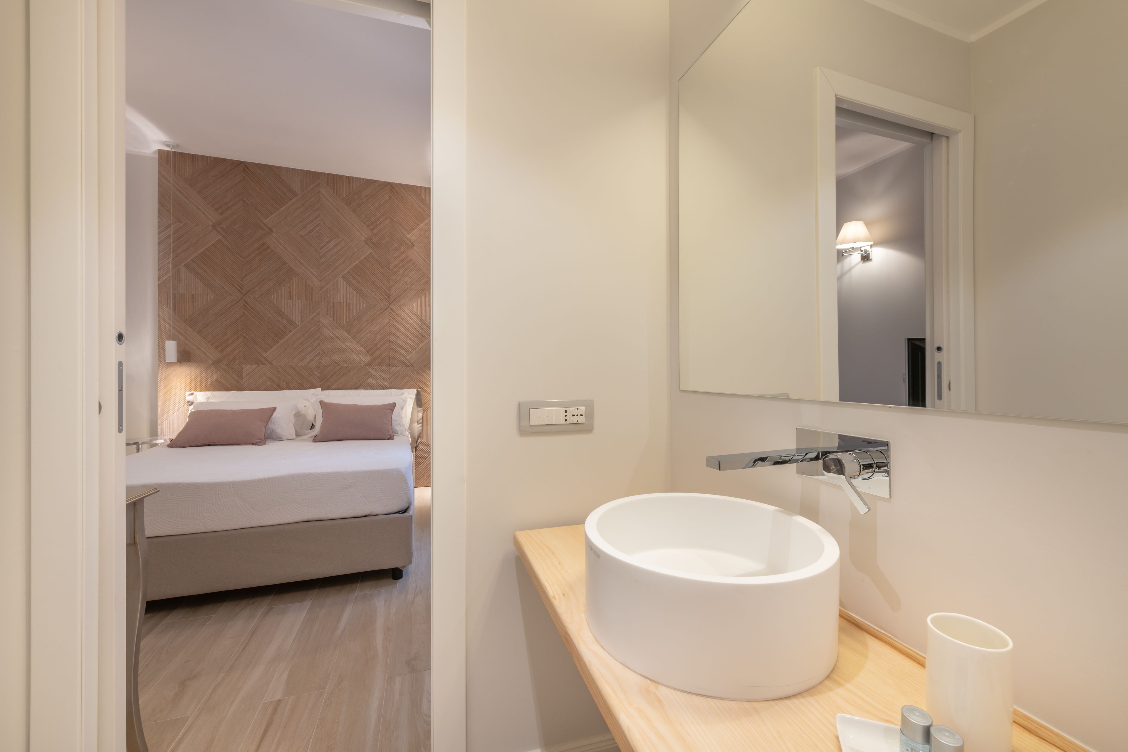 Une chambre à coucher moderne avec un lit, un grand miroir et un lavabo blanc.