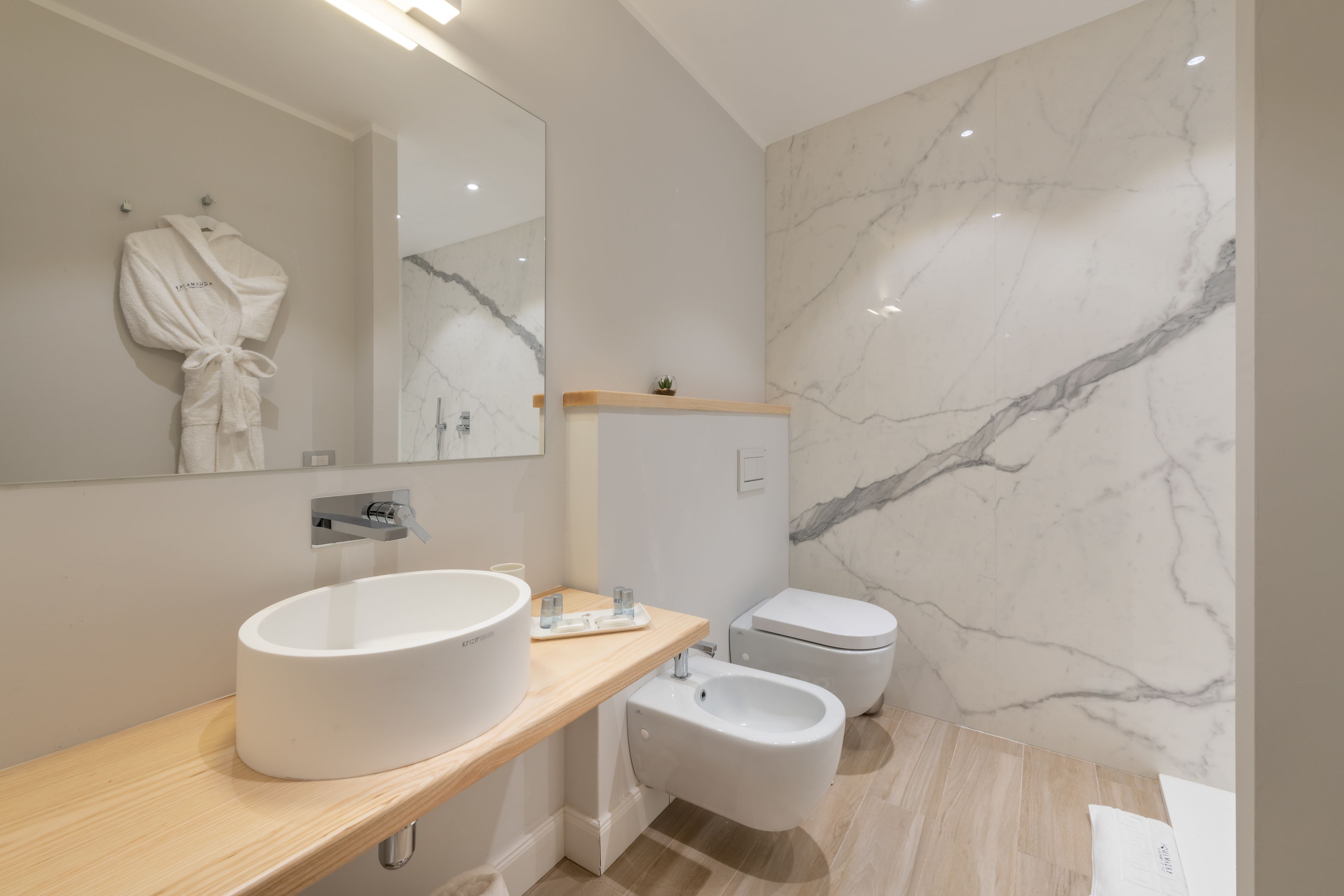 Et moderne badeværelse med et stort spejl, en rund vask, en bidet og et toilet.