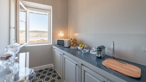 Una cocina con ventana, microondas, tabla de cortar y frutero.
