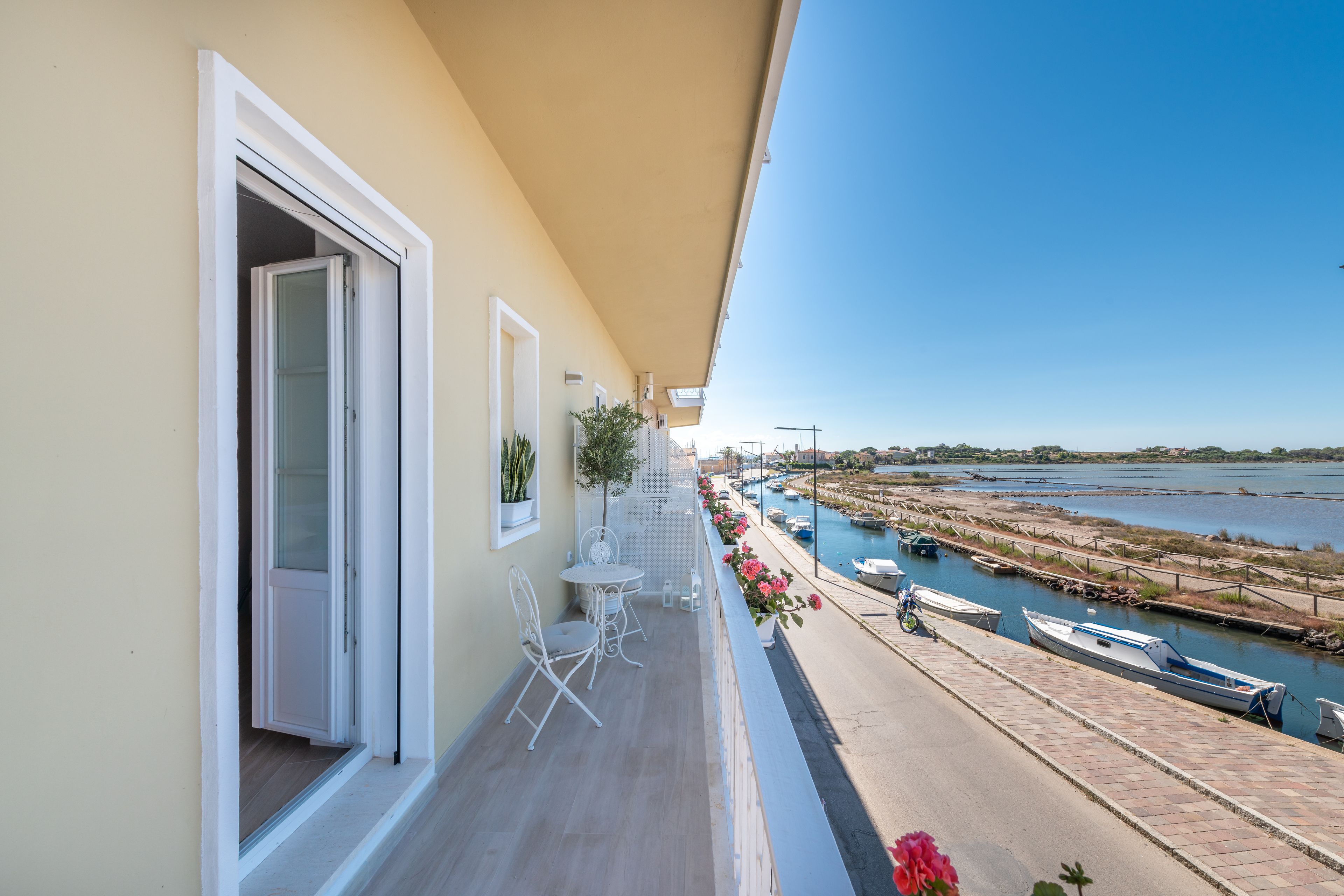 A balcony with a view of a river and boats, a small table and chairs, and a potted plant.