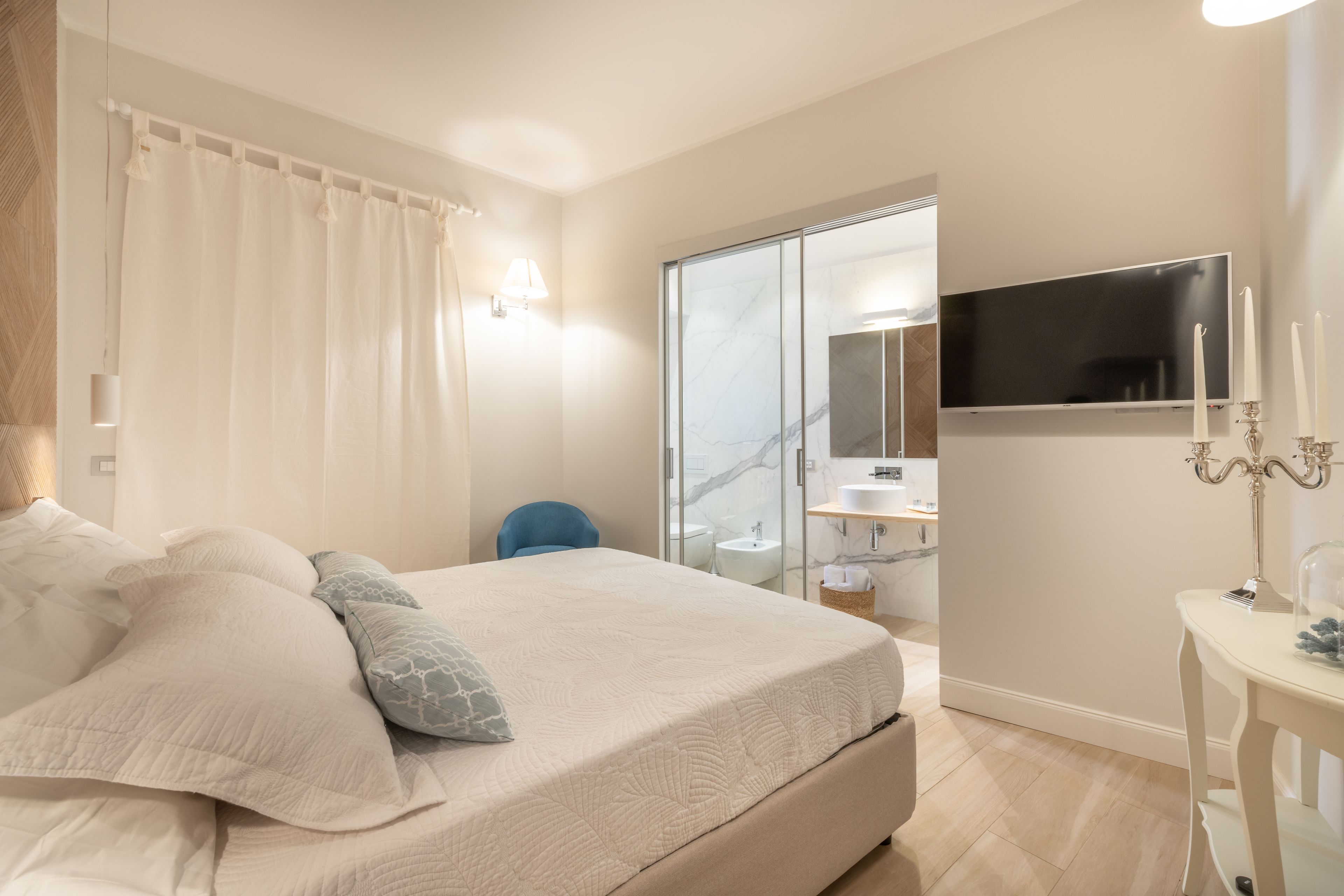 A bedroom with a bed, a TV, a bathroom with a mirror, and a bedside table with a lamp.