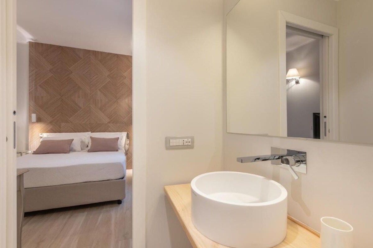 A modern bedroom with a bed, a wooden headboard, a large mirror, and a round white sink.