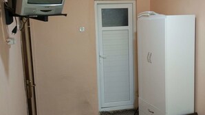 Une petite pièce avec un téléviseur fixé au mur, une armoire blanche et un lit recouvert d’une couvre-lit à motifs floraux.