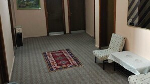 Un couloir avec un tapis à motifs, un tapis rouge et bleu, une table blanche recouverte d’une nappe à motifs et deux portes en arc de cercle.