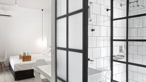 Ett modernt hotellrum med ett stort fönster, en säng, ett skrivbord och ett badrum med dusch.