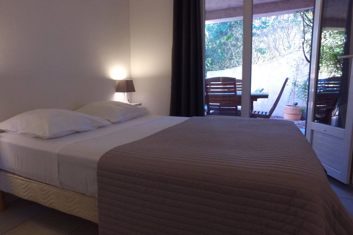 A bedroom with a bed, bedside lamps, and a view of an outdoor area with a table and chairs.
