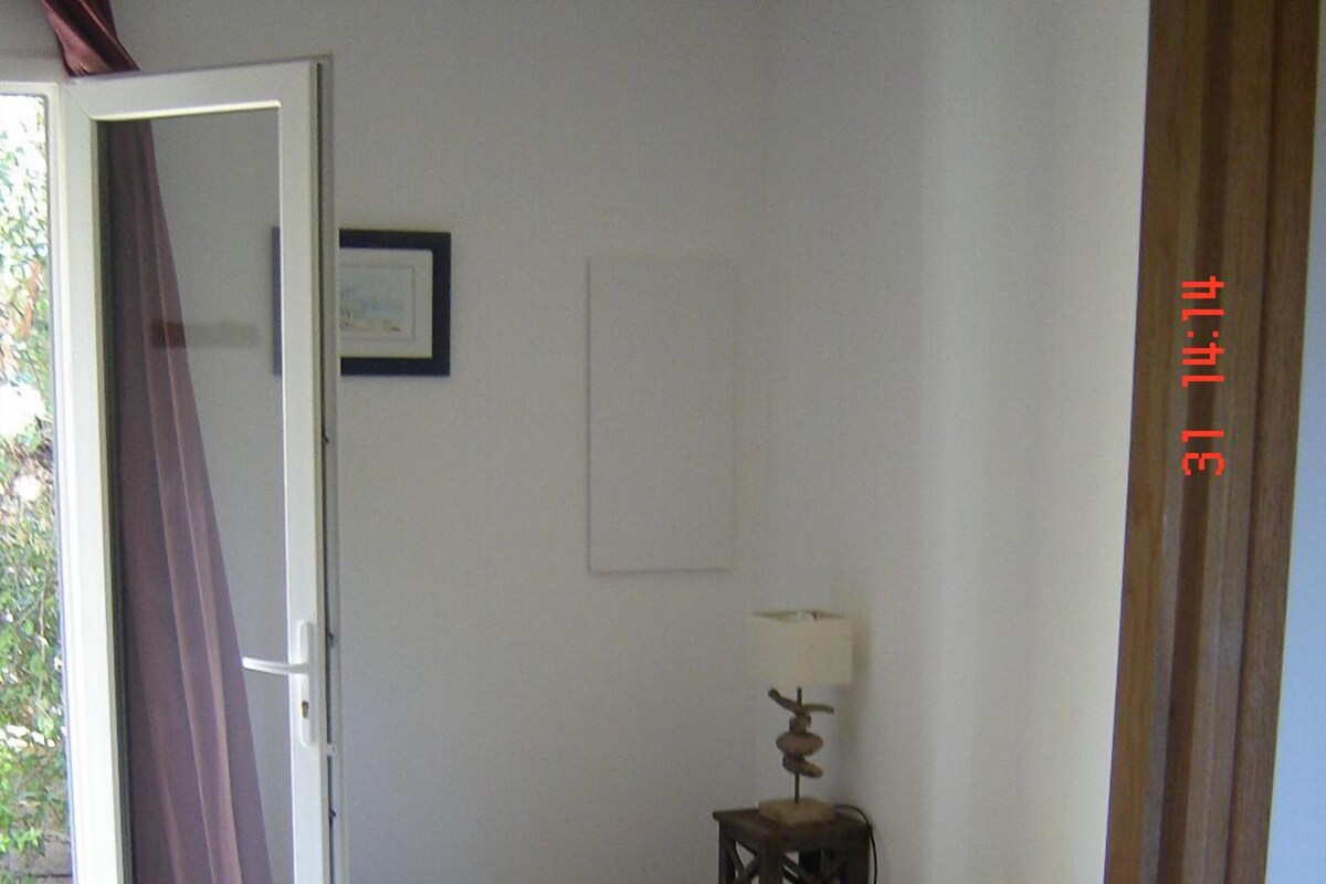 A bedroom with a bed, a small table with a lamp, a door, and a picture on the wall.