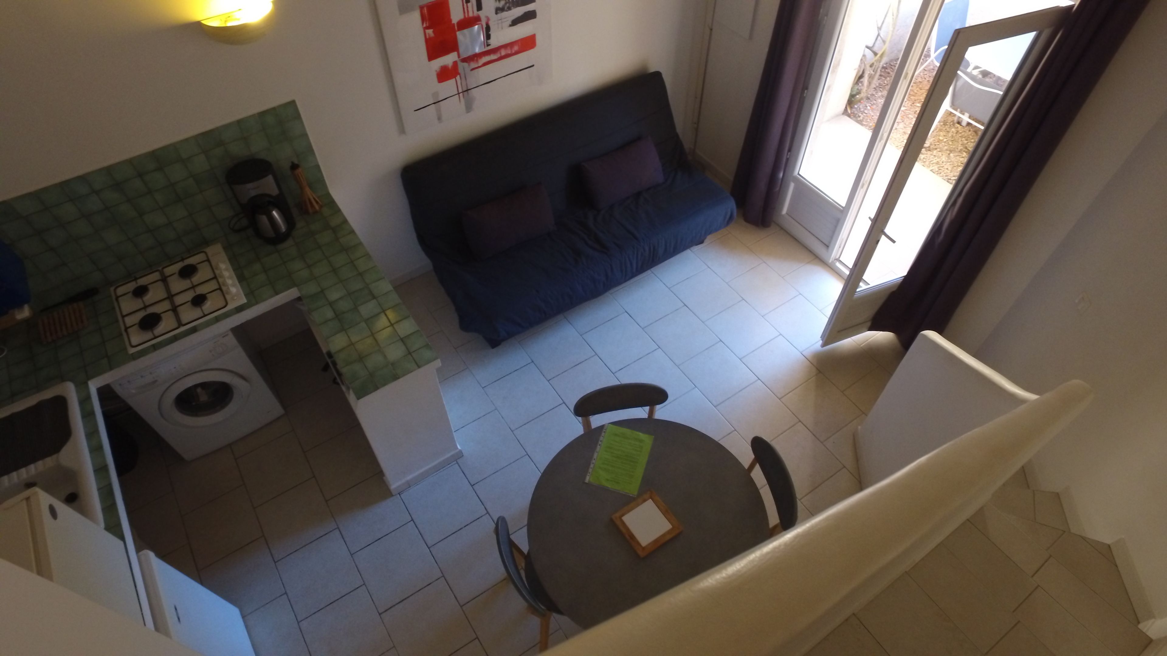 Un espace de vie compact comprenant un coin cuisine, un canapé, une table à manger et un escalier.