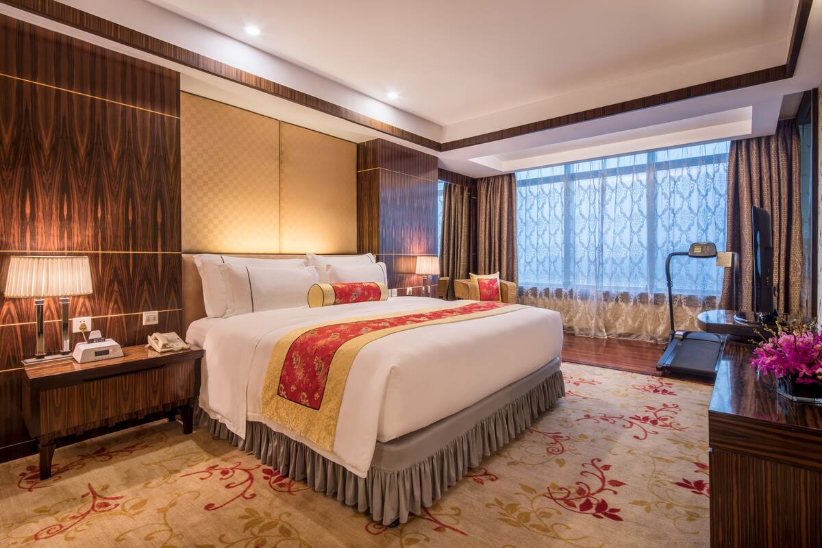 Een hotelkamer met een groot bed, een bureau met een lamp, een telefoon en een raam met gordijnen.