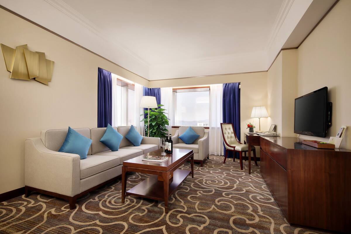 Een hotelkamer met een bank, een bijzettafeltje, een bureau met een televisie en een kamerbreed tapijt met een patroon.