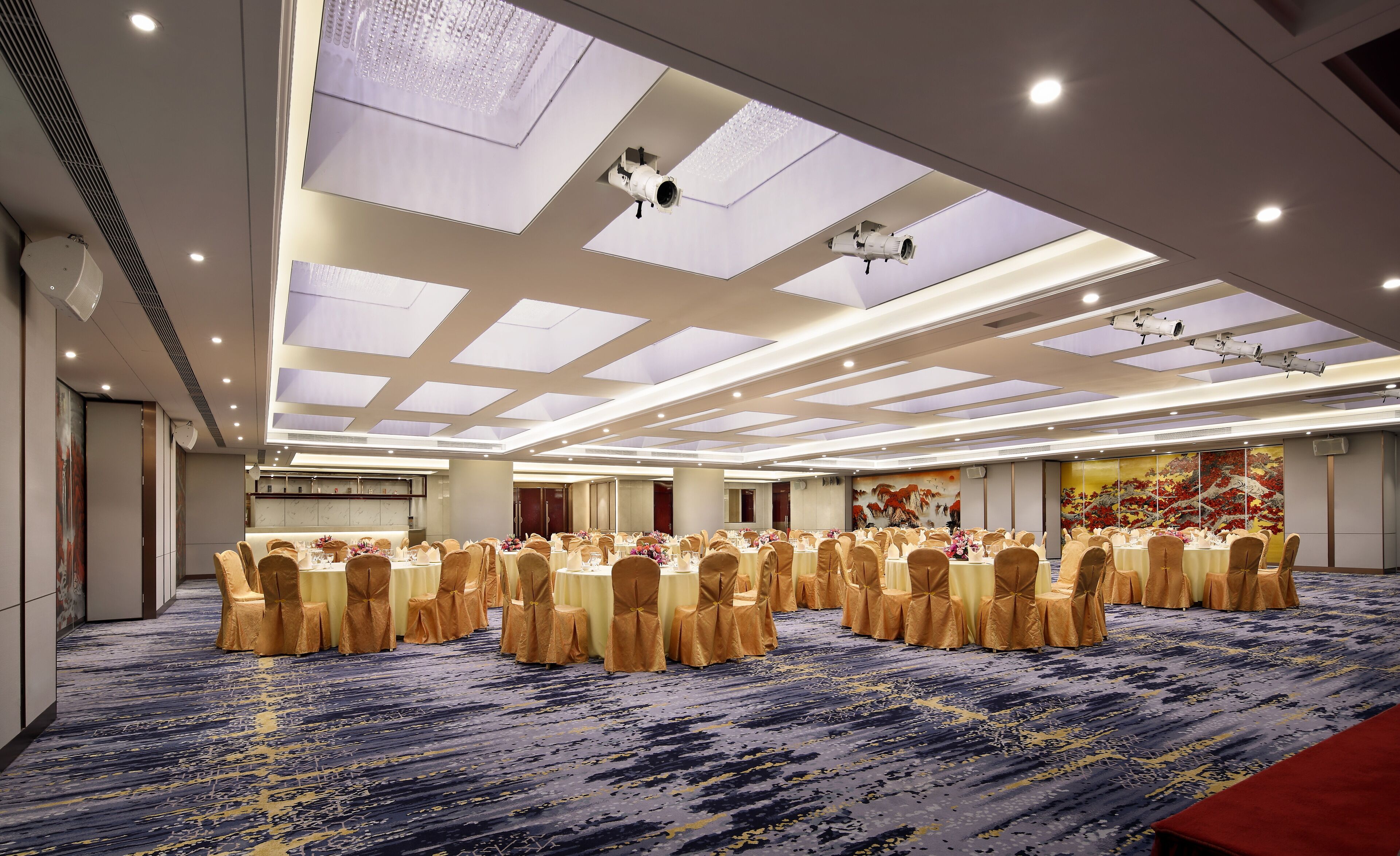 Un amplio salón de conferencias con mesas redondas, sillas doradas y una alfombra estampada.