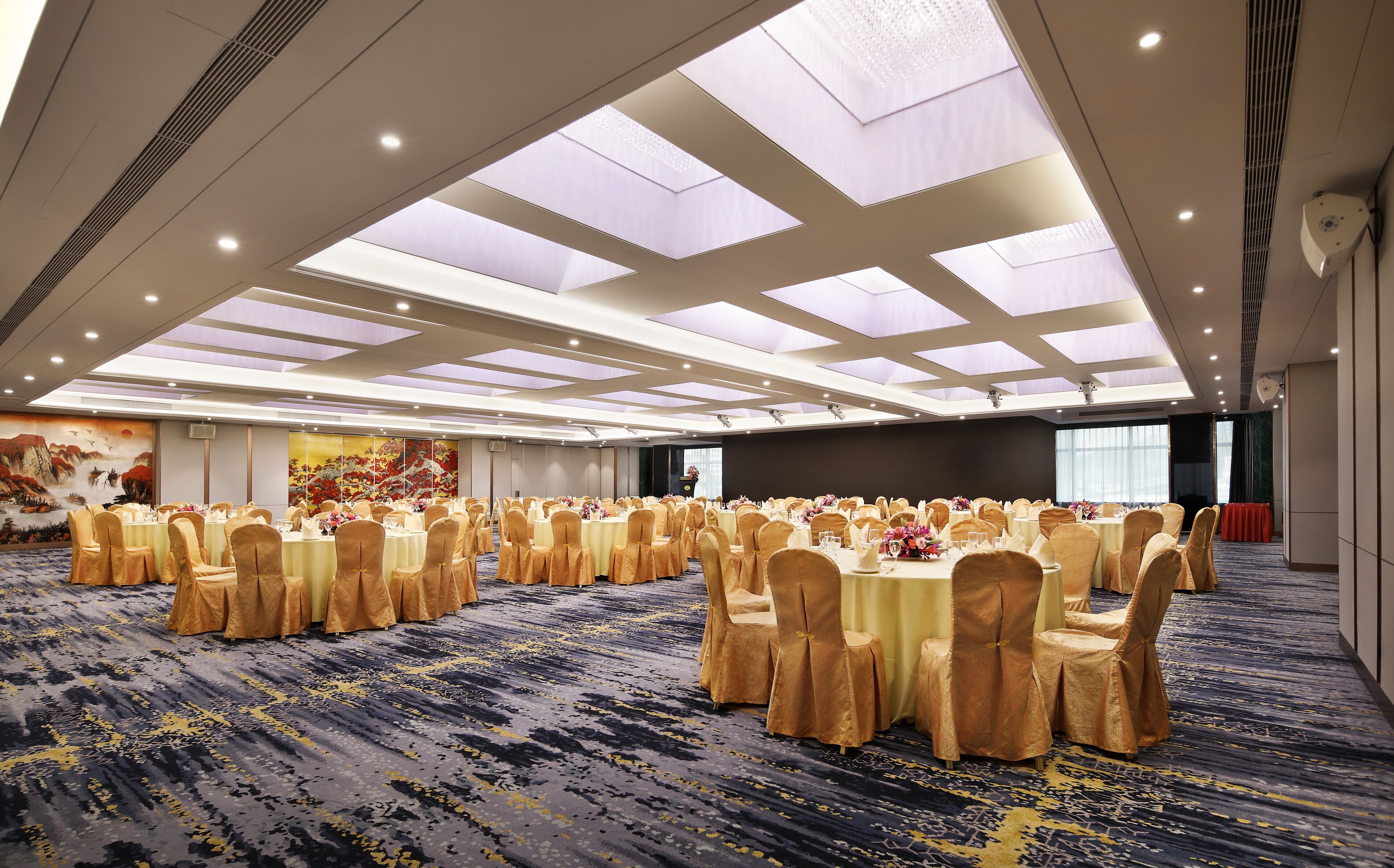 A large banquet hall with round tables, gold chairs, and a patterned carpet.
