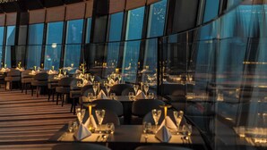 A restaurant with tables set for dining, large windows, and a view of the cityscape.