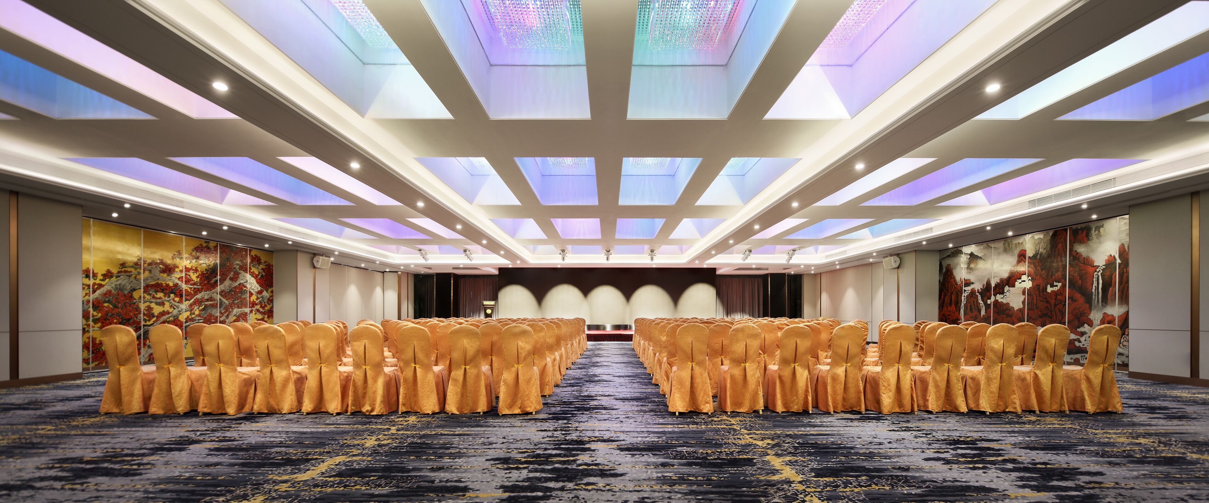 Un salón de conferencias con filas de sillas, suelo alfombrado y un techo con tragaluces.