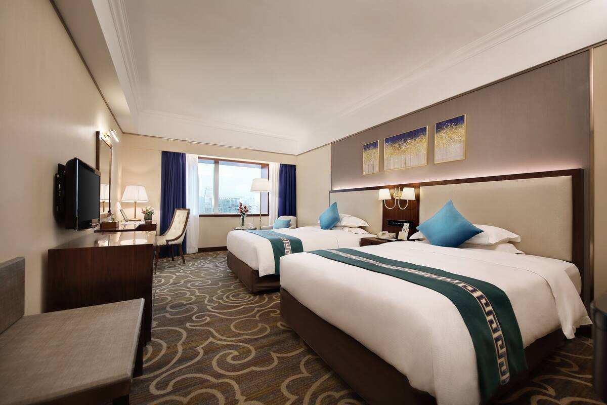 Hotelkamer met twee bedden, een bureau met televisie, een stoel en uitzicht op de stad.