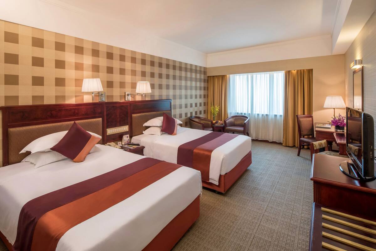 Een hotelkamer met twee bedden, een bureau, een stoel, een televisietoestel en een raam met gordijnen.
