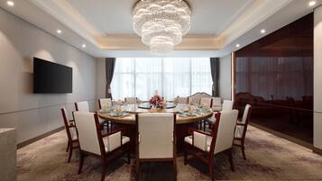 A conference room with a round table, chairs, a chandelier, a flat-screen TV, and a large window.