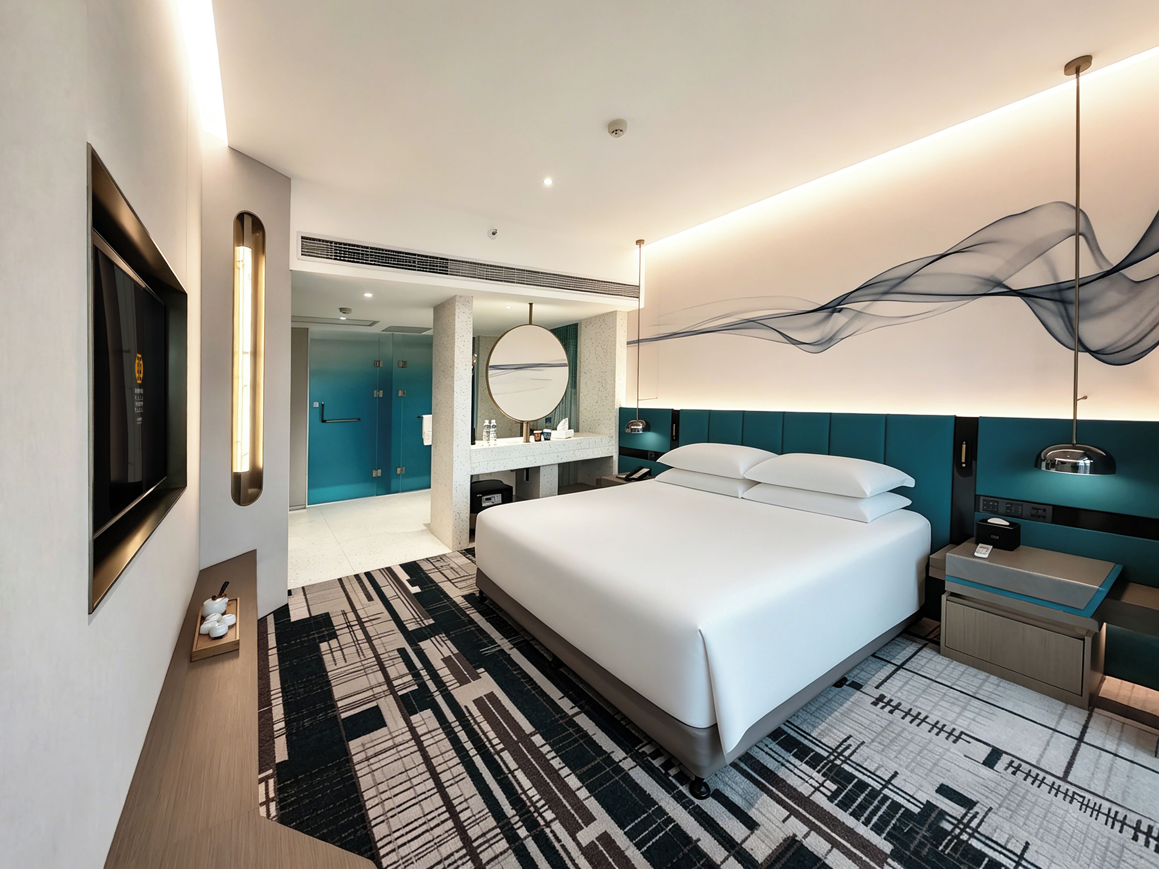 A modern hotel room with a large bed, a bathroom with a mirror, and a TV mounted on the wall.