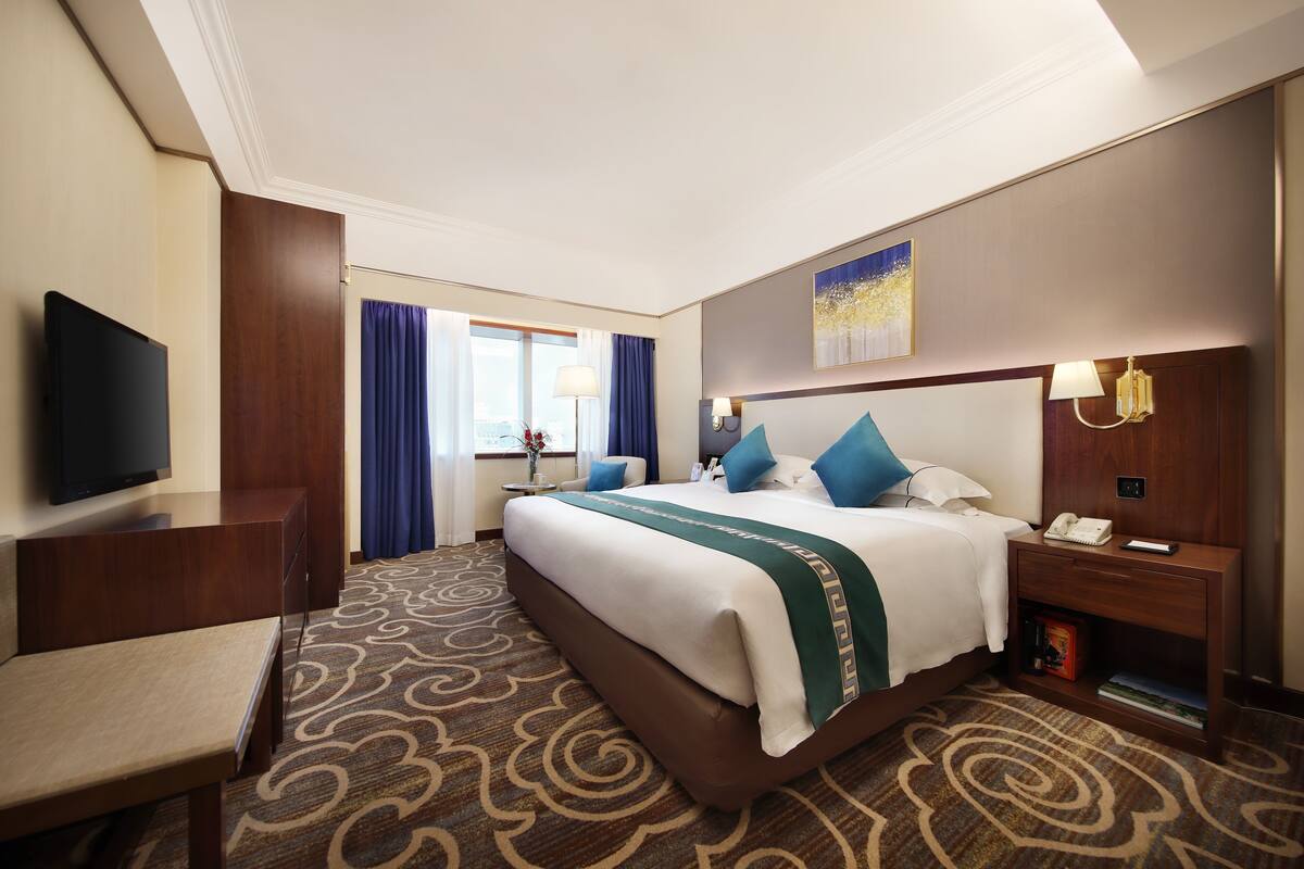 Een hotelkamer met een bed, een bureau, een televisie, een nachtkastje en een raam met gordijnen.