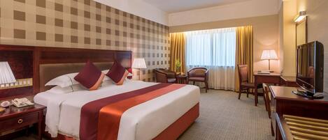 A hotel room with a large bed, a desk, a chair, a television, and a window with curtains.