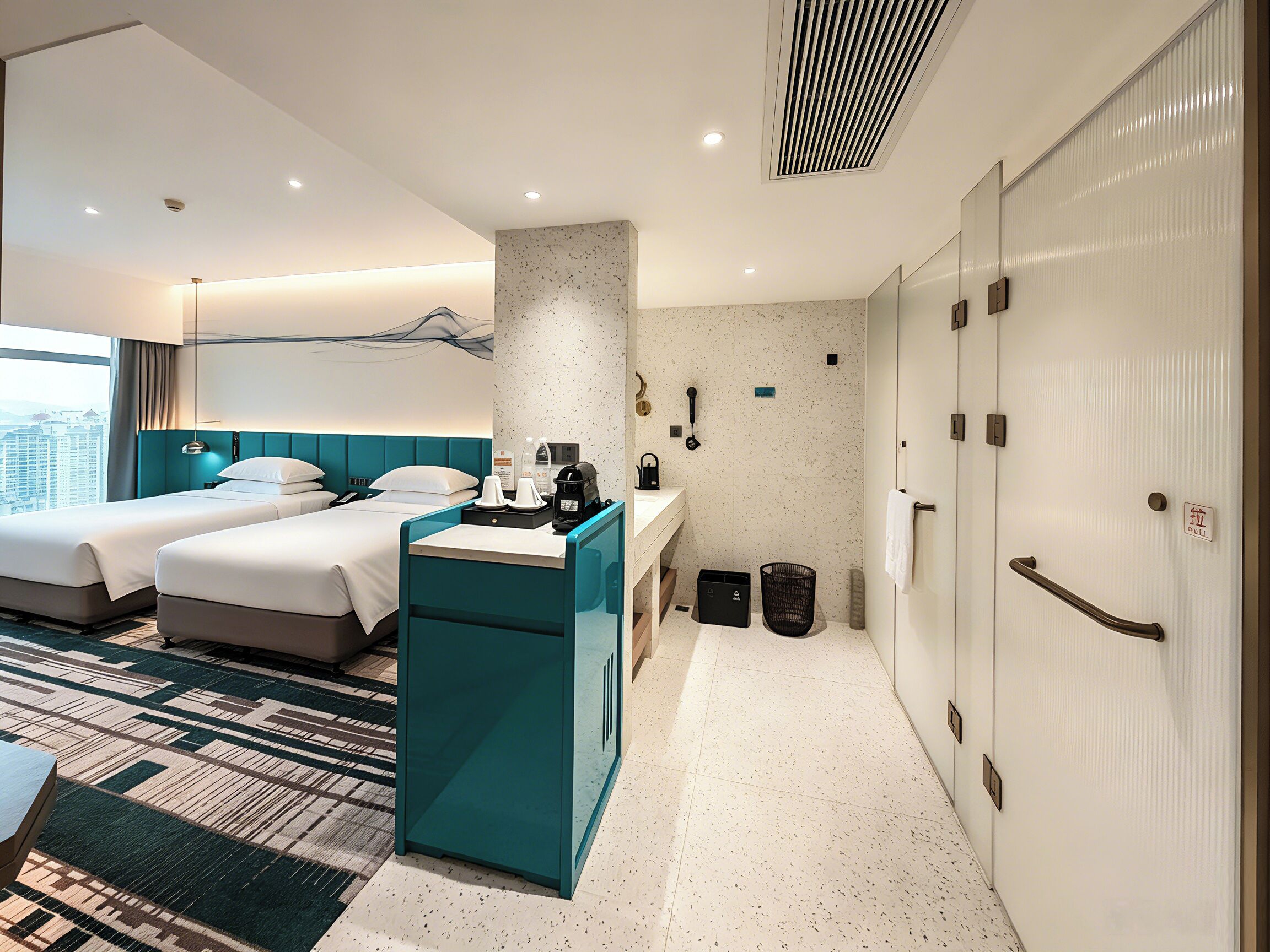 Habitación de hotel con dos camas, un escritorio, baño y vista a la ciudad.