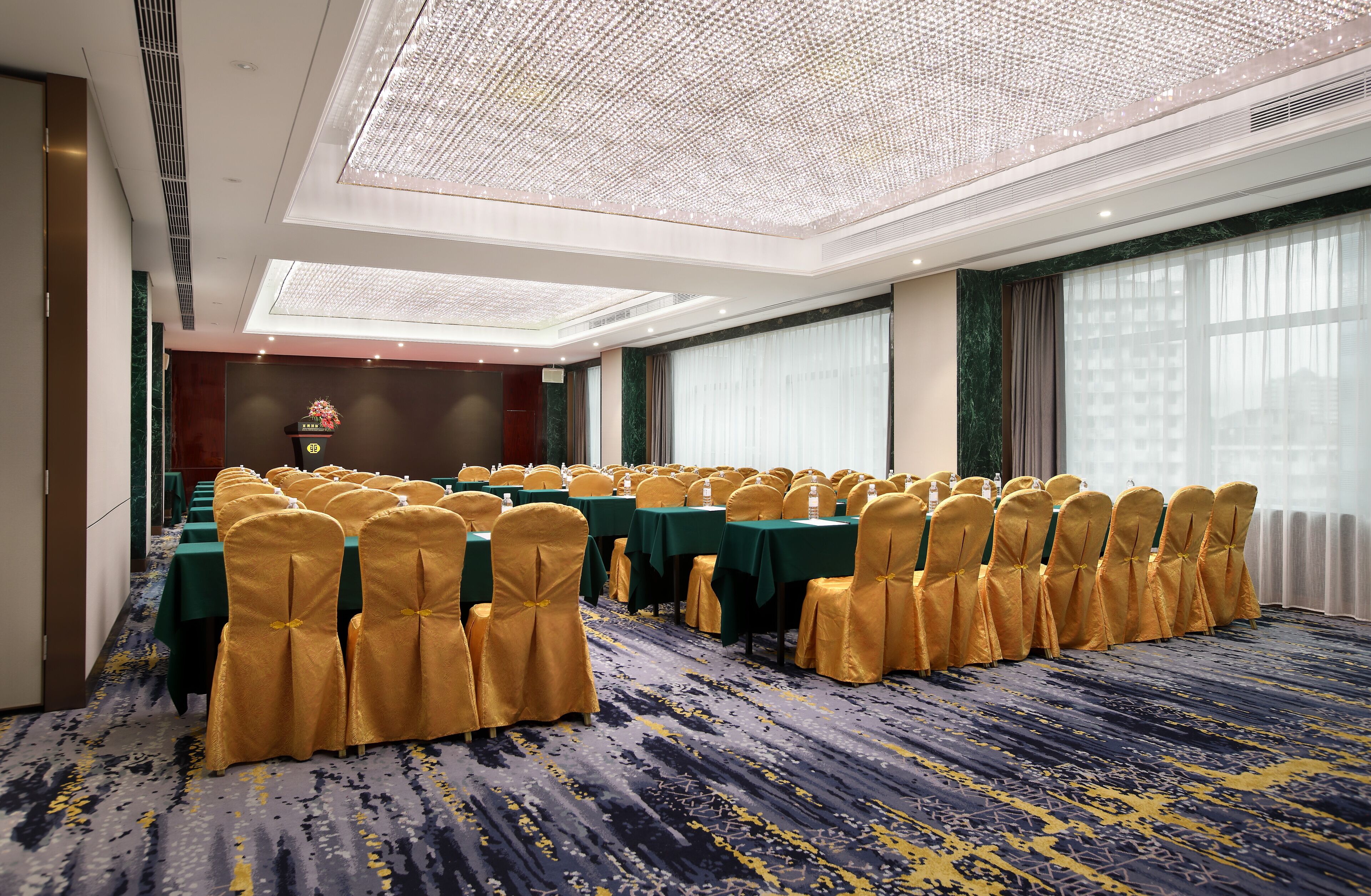 Un salón de conferencias con filas de mesas y sillas, un candelabro y un ventanal grande.