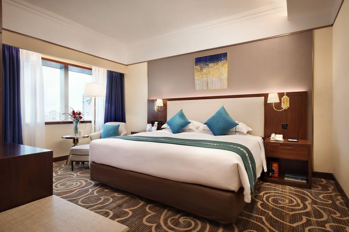 Een hotelkamer met een groot bed, een bureau, een stoel, een lamp en een nachtkastje met een telefoon.