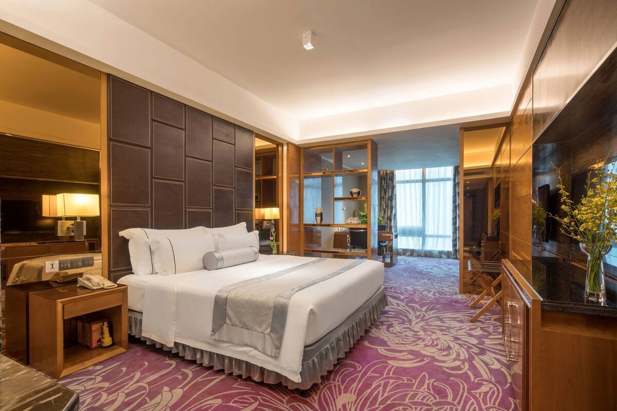 Een hotelkamer met een groot bed, een bureau, een stoel, een televisie en een badkamer die door een open deur zichtbaar is.