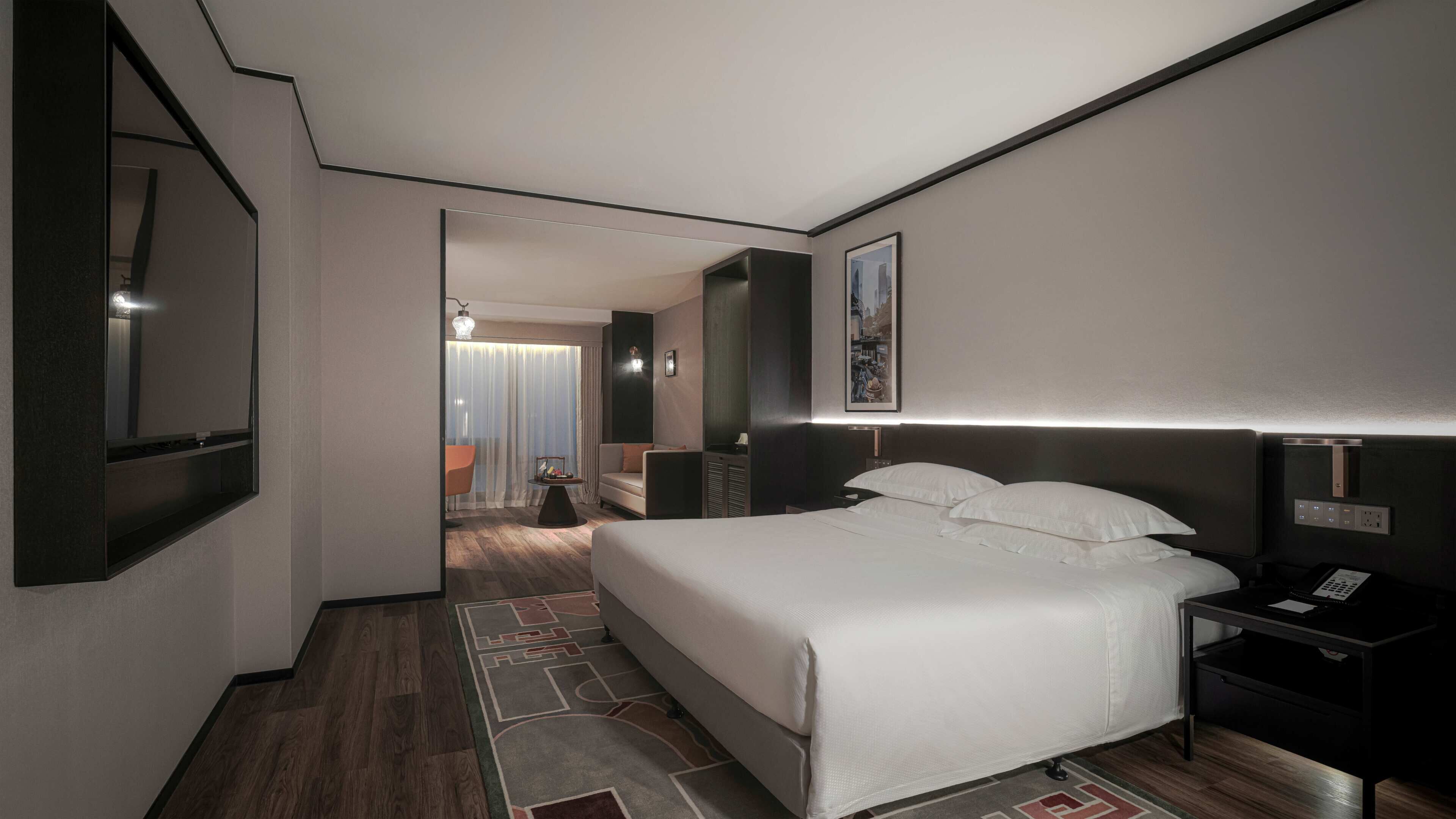 A hotel room with a large bed, bedside tables, a flat-screen TV, and a view of the hallway.